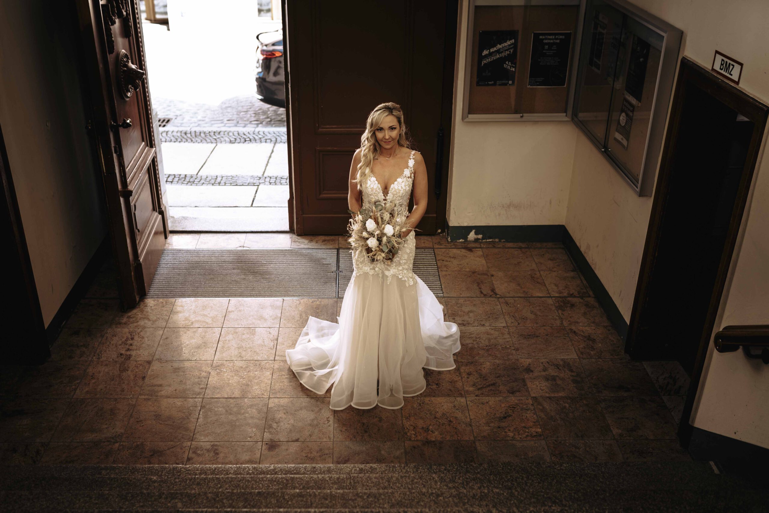 Braut mit Blumenstrauß im Hochzeitskleid Braut in einem eleganten Hochzeitskleid mit Blumenstrauß, steht auf einer Treppe in einem historischen Gebäude.
