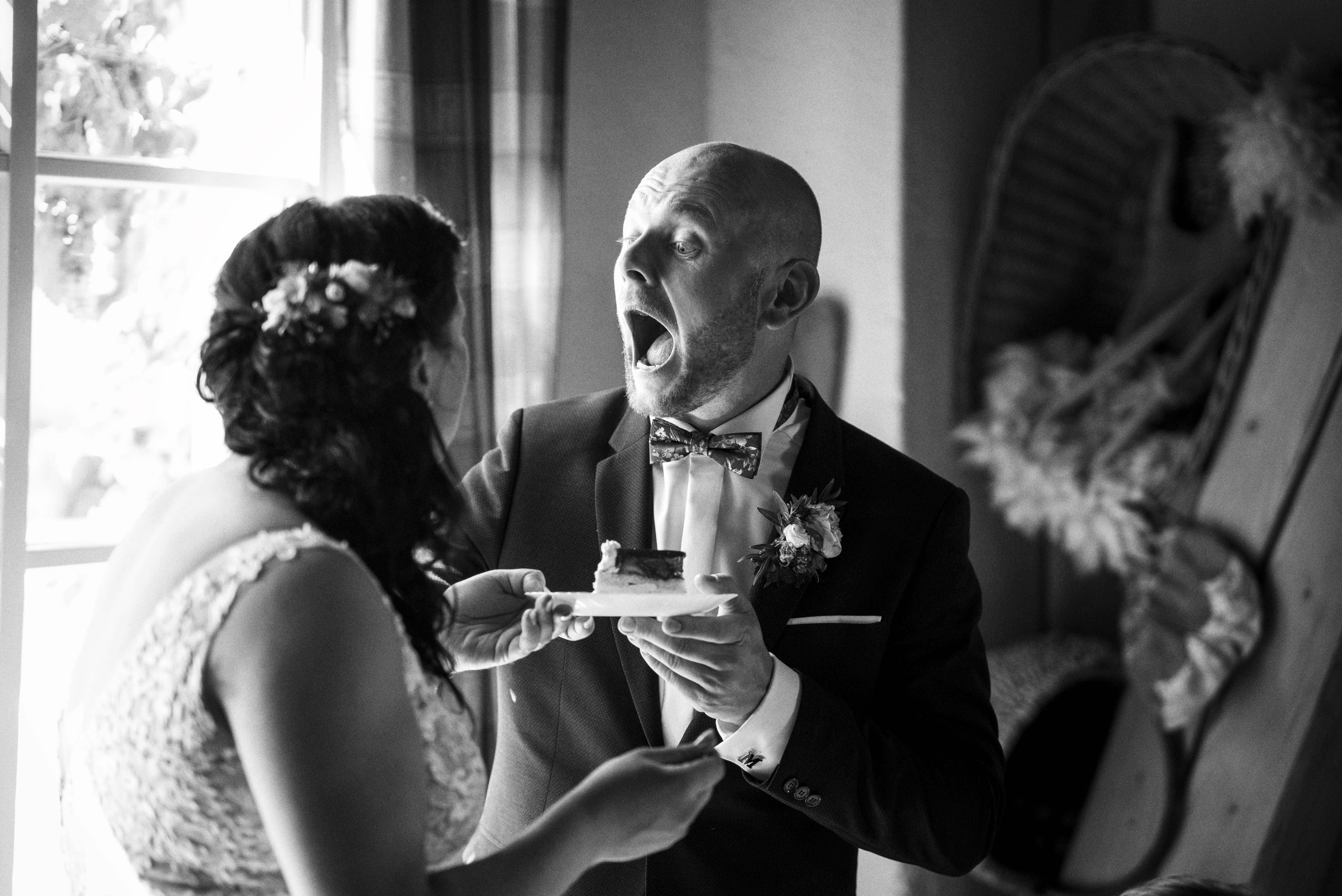 Ein Brautpaar in festlicher Kleidung, der Bräutigam zeigt Überraschung, während er ein Stück Kuchen von der Braut erhält. Hochzeitsfeier-Moment. Foto: Roman Koryzna