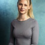 Junge Frau mit langen blonden Haaren in einem grauen Oberteil, sitzend vor einem blauen Hintergrund. Fotograf: © Roman Koryzna, Bewerbungsfoto, Studio Koryzna, Fotostudio, Radibor, Bautzen