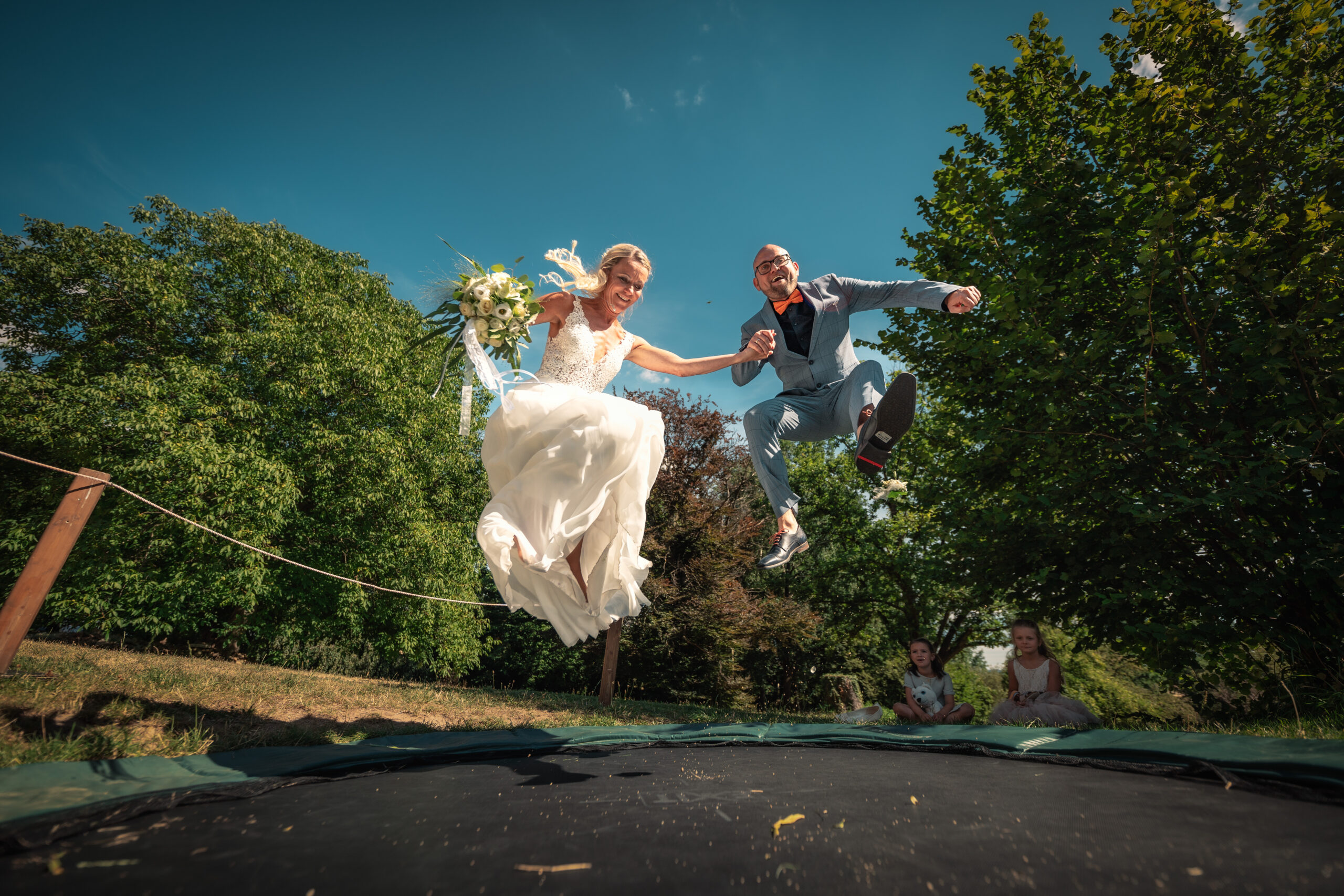 Hochzeitsfeier mit Braut und Bräutigam auf einem Trampolin Braut und Bräutigam springen gemeinsam auf einem Trampolin in einem Garten. Foto: © Roman Koryzna, Hochzeitsfotograf. Weißenberg 2022. Hochzeitsfotograf für Bautzen Dresden und die Lausitz.
