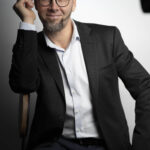 Mann mit Glatze und Brille, der in einem Anzug sitzt und lächelt. Fotograf: © Roman Koryzna, Businessfotos, Studio Koryzna, Radibor, Bautzen