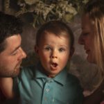 Ein Familienporträt mit einem Kleinkind, das überrascht aussieht, während es von den Eltern umgeben ist. Fotograf: © Roman Koryzna, Familienfoto, Studio Koryzna, Fotostudio, Radibor, Bautzen