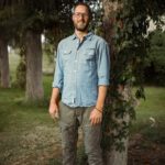 Mann in einem blauen Hemd und grünen Hosen steht lächelnd neben einem Baum. Fotograf: © Roman Koryzna, Bewerbungsfoto, Studio Koryzna, Radibor, Bautzen