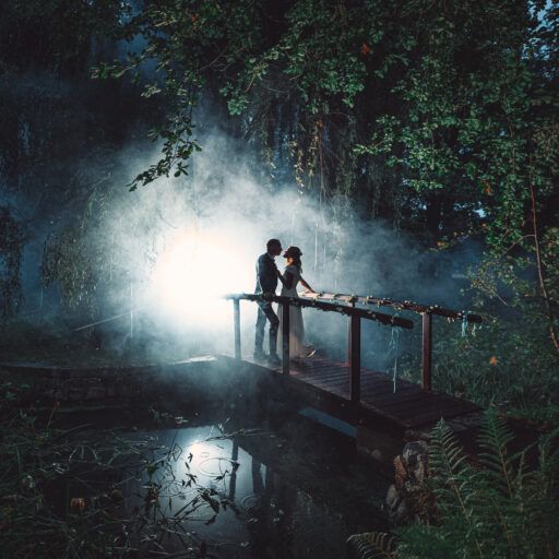 Paar steht auf einer Brücke in einem nebligen Wald mit Licht im Hintergrund. Foto: © Hochzeitsfotograf Roman Koryzna, August 2022. Hochzeitsfotograf für Bautzen und Dresden